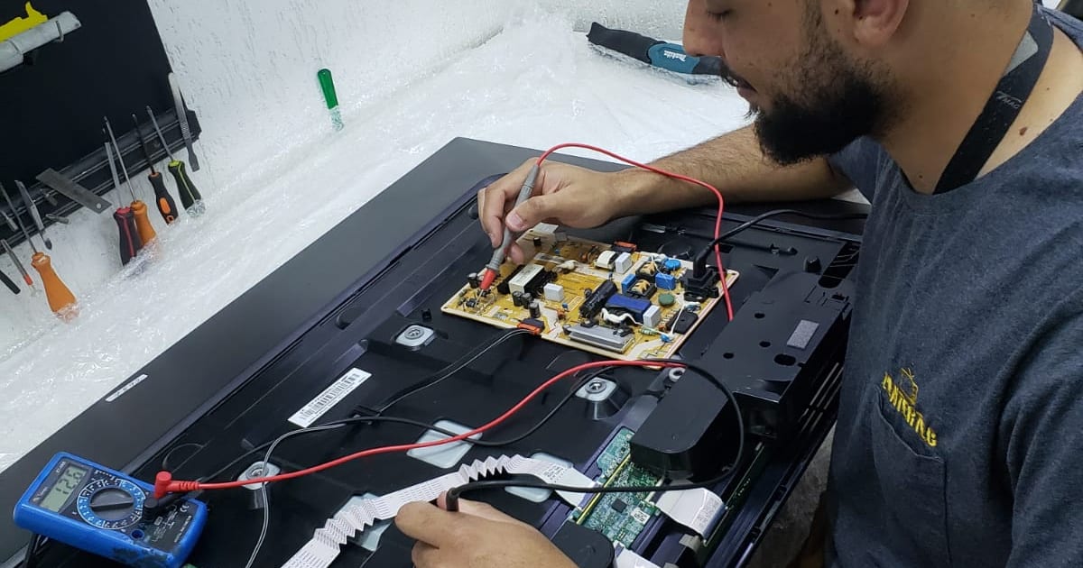 Técnico da Centertec medindo a placa de fonte de uma TV aberta com multímetro