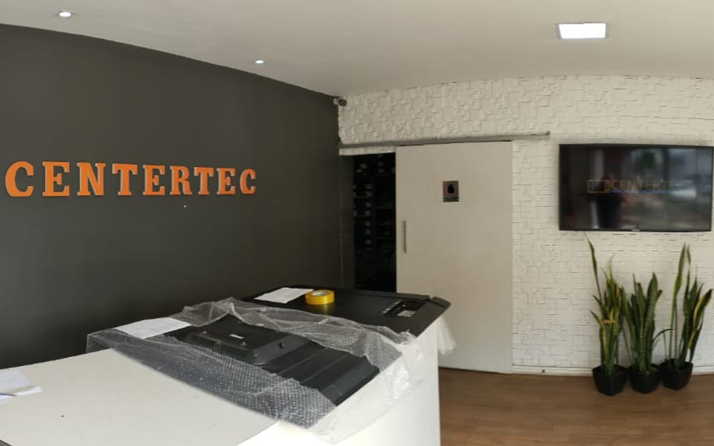 Interior da loja Centertec, com balcão de atendimento e TV na parede