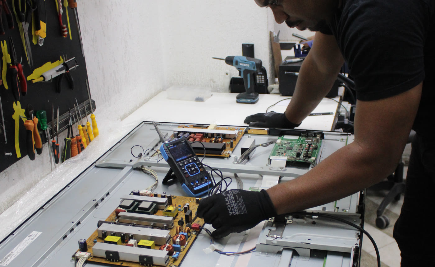 Técnico da Centertec medindo com osciloscópio as placas de uma TV aberta na bancada